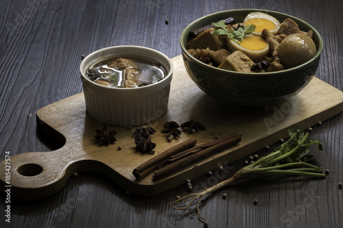 Eggs and sweet pork with fried tofu, boiled in brown sauce and in white bowl on old brown wooden plank (Thai food called 