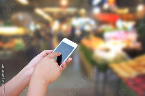 blurred  hand and touch screen smart phone on people in food center with light bokeh.