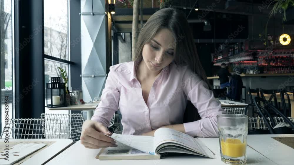 Young student girl reading coursebook by table at cafe
