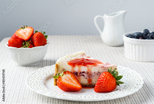 Delicious cheesecake with strawberry on a table against white wall.