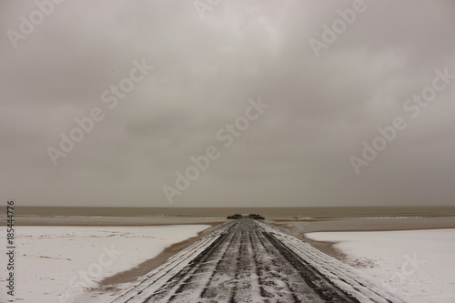 Winter beach and pier in snow on cloudy day at Northern sea, Belgium, Blankenberge. Severe weather on seacoast. Perspective landscape. Winter seashore. Travel and loneliness background. photo