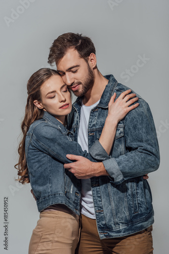 beautiful happy young couple with closed eyes hugging isolated on grey