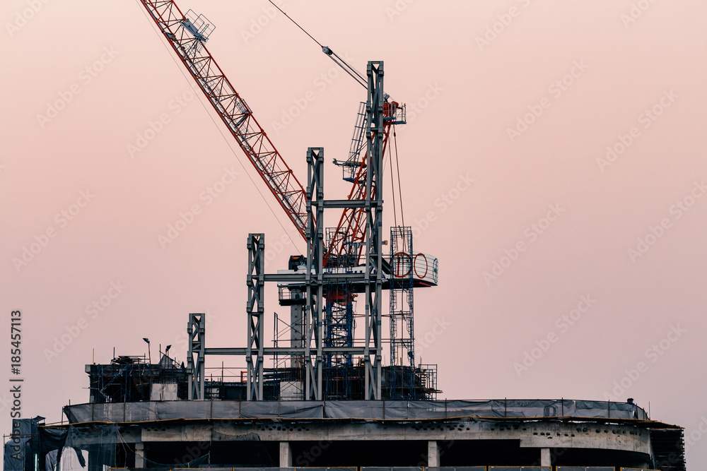 cranes on top of under construction high-rise building at twilight cranes on top of under construction high-rise building at twilight