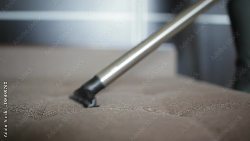 Housework and housekeeping concept - a woman with a vacuum cleaner cleans the sofa Housework and housekeeping concept - a woman with a vacuum cleaner cleans the sofa