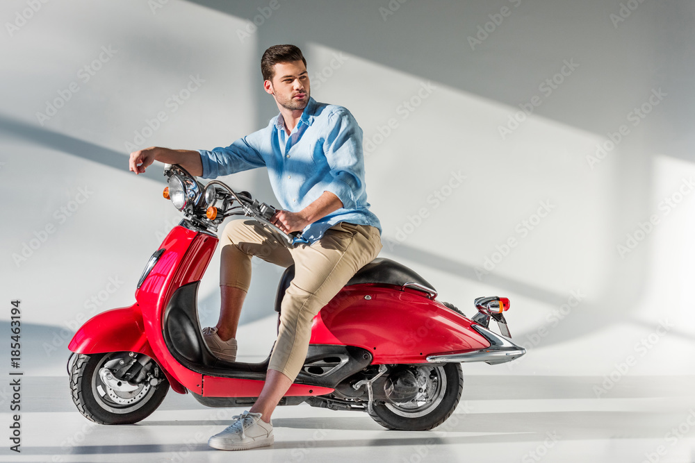 side view of young pensive man looking away while sitting on red scooter