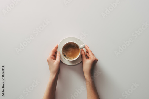 top view of female hands and cup of coffee with saucer on grey