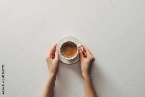 Obraz top view of female hands and cup of coffee with saucer on grey