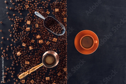 top view of cup of coffee with saucer, roasted coffee beans, brown sugar, coffee pot and scoop on black