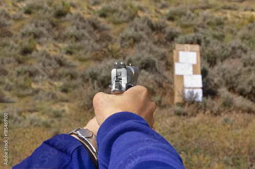 1911-type semi-automatic pistol in a two-hand hold aimed at a cardboard target on an outdoor range photo