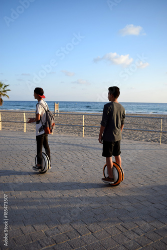 Boys are enjoying riding Monowheels scooters on a beach promenade photo