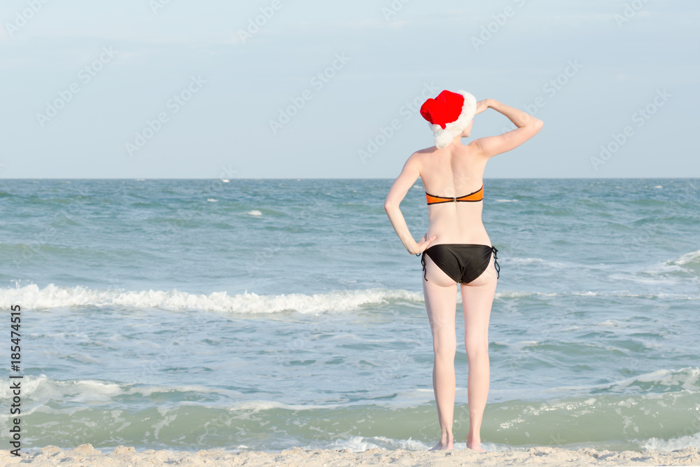 Girl in Santa hat and bathing suit looks into the distance. Sea shore. Girl in Santa hat and bathing suit looks into the distance. Sea shore.