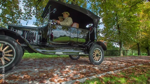 Elegantly dressed driver behind the steering wheel driving special wooden car Ford model T, that originates from USA.