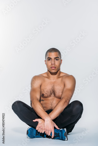 shirtless african american sportive man stretching legs on floor