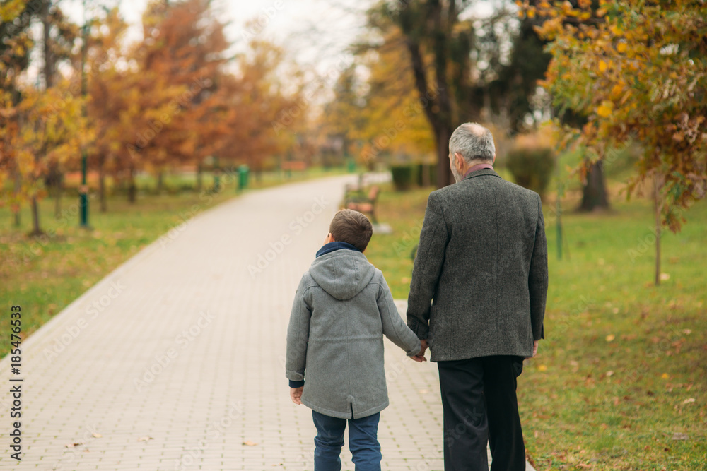 Fototapeta premium Grandpa and his grandson spend time together in the park. They are sitting on the bench. Walking in the park and rejoicing