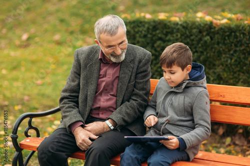 Grandpa and his grandson spend time together in the park. They are sitting on the bench. Walking in the park and rejoicing
