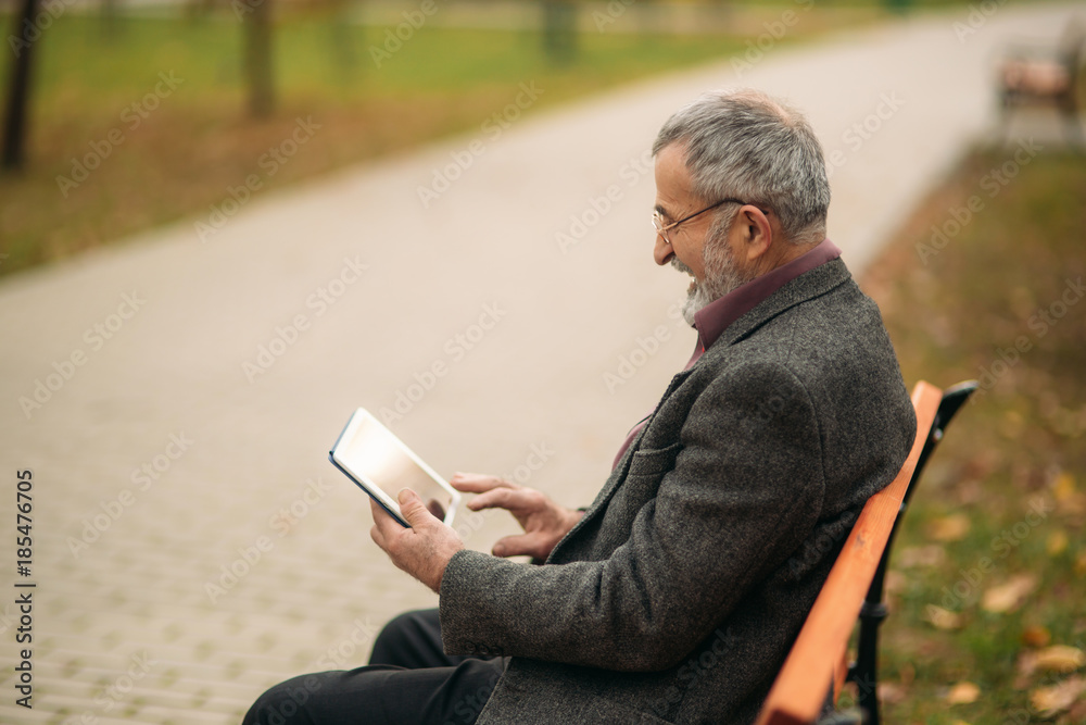 Grandpa use a tablet sitting in the pakr on the bench Grandpa use a tablet sitting in the pakr on the bench