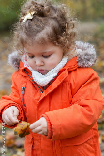 Autumn outdoor games. Cute toddler girl is holding a leaf.  