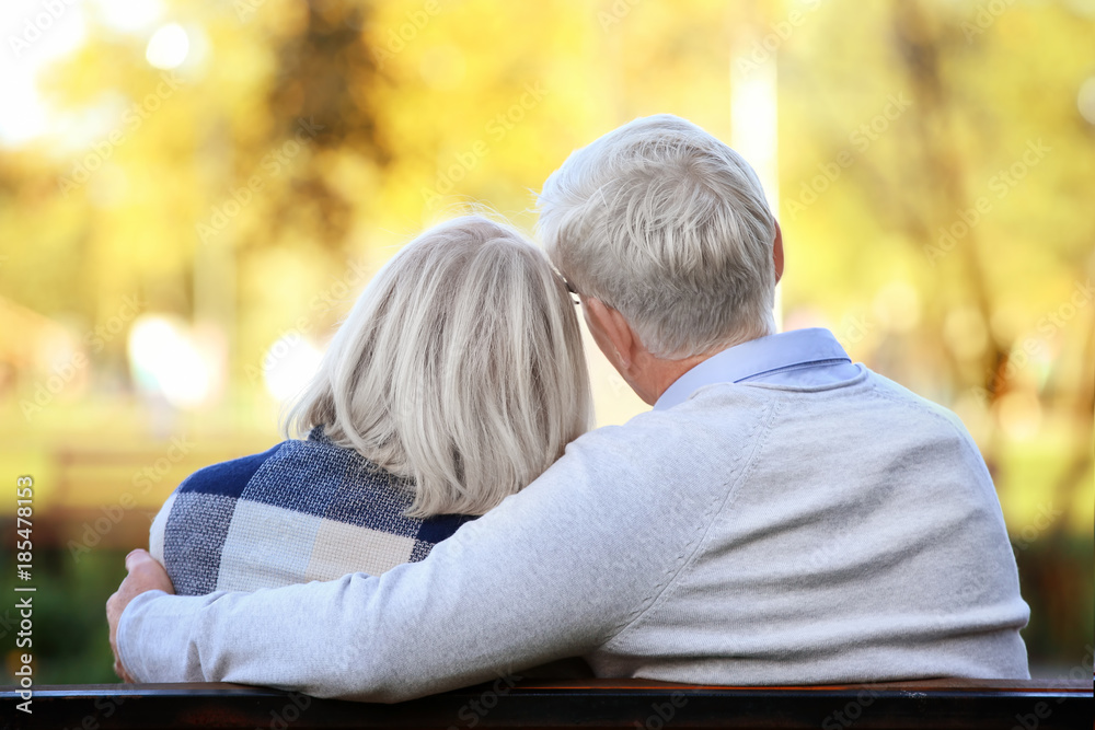 Cute elderly couple sitting on bench in autumn park Cute elderly couple sitting on bench in autumn park