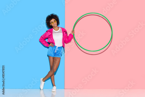 Woman in sportswear standing with hoop in hand on pink and blue background © LIGHTFIELD STUDIOS