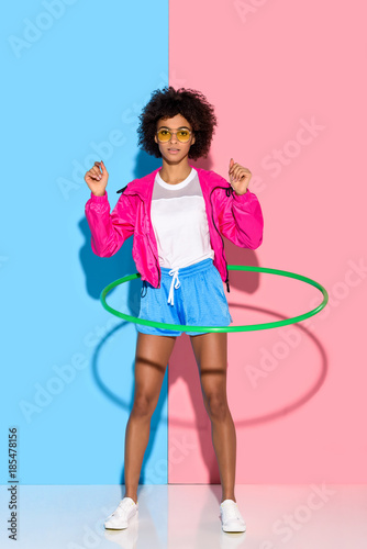 Sporty woman posing while exersizing with hoop and looking at camera on pink and blue background © LIGHTFIELD STUDIOS