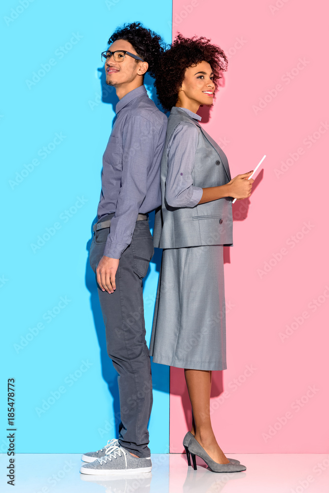 Young african amercian businessman standing by businesswoman with tablet in hands on pink and blue background Young african amercian businessman standing by businesswoman with tablet in hands on pink and blue background
