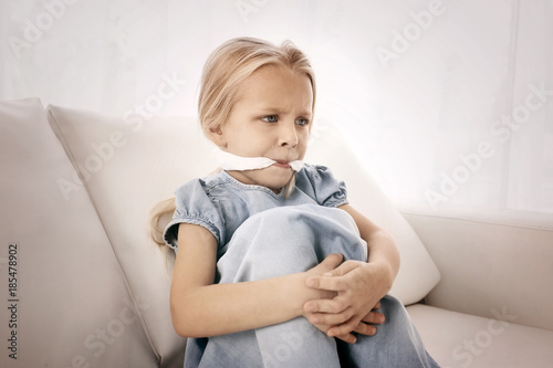 Helpless little girl with gag in mouth indoors. Child abuse concept