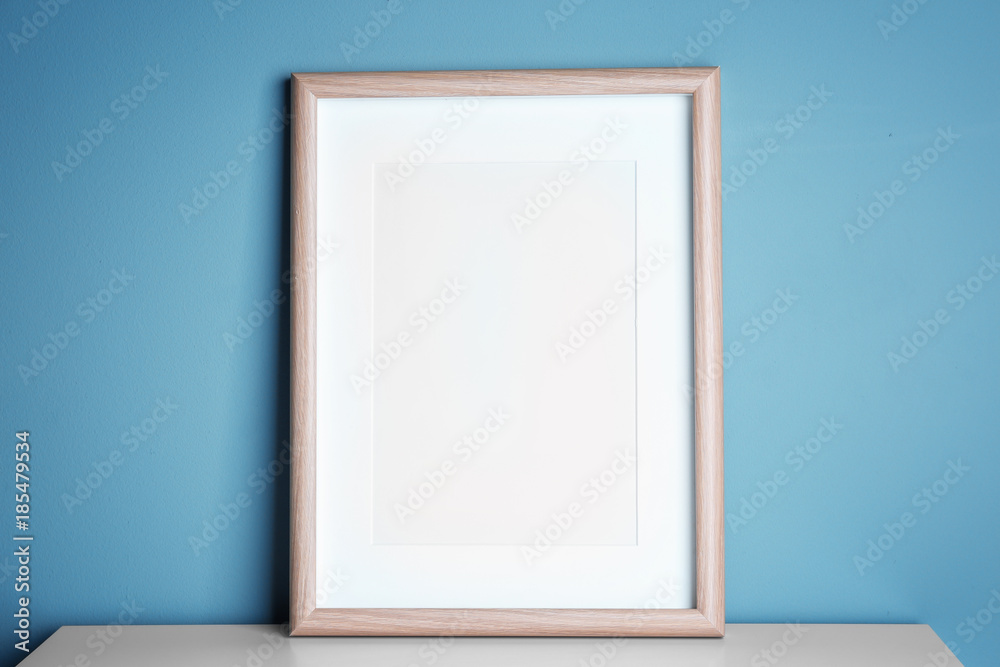 Empty wooden frame on table near color wall Empty wooden frame on table near color wall