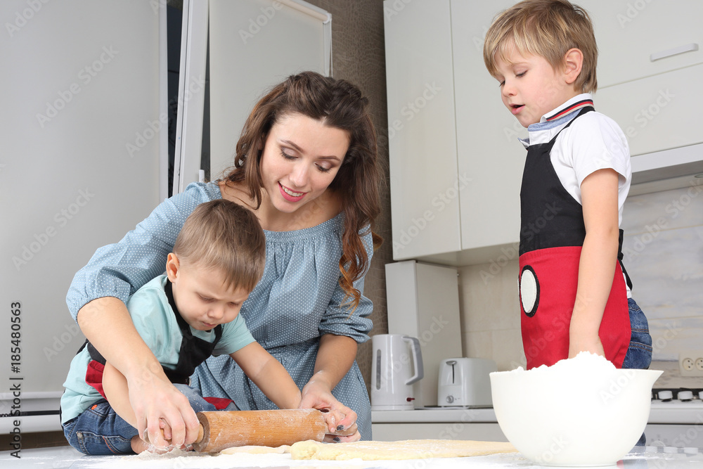 mom helps young sons knead the dough on the kitchen table.