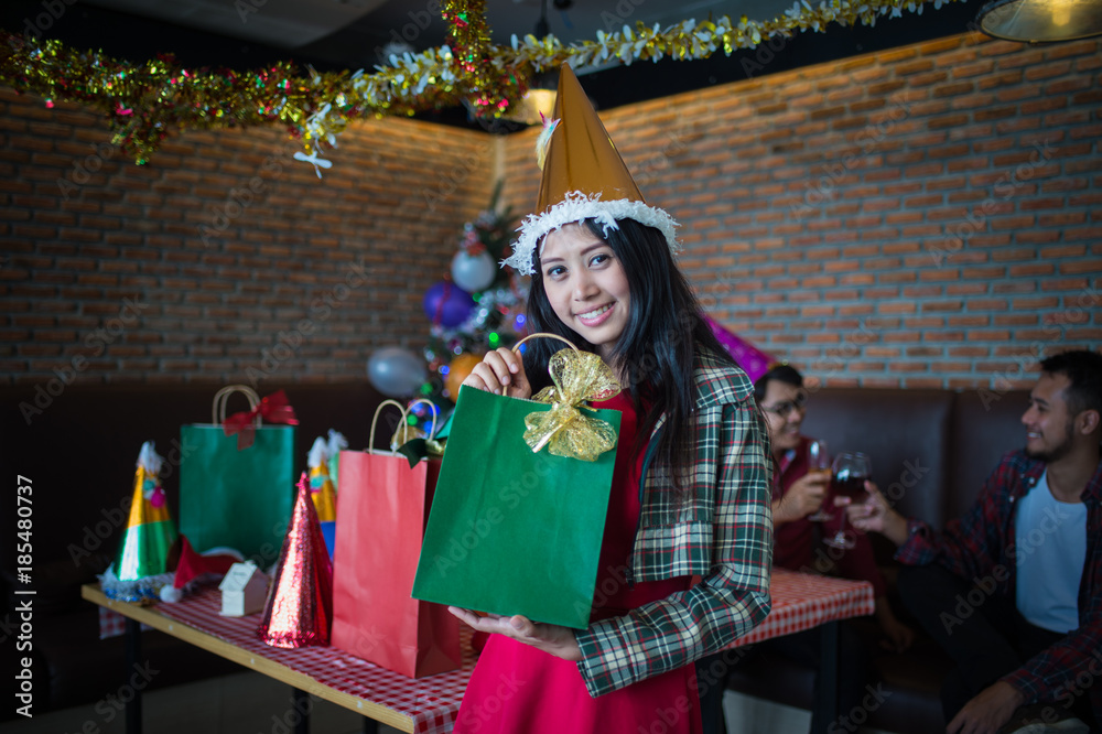 beautiful woman wear red dress and santa claus hat showing green gift bag on hand in restaurant. concept of Christmas party and New year party. beautiful woman wear red dress and santa claus hat showing green gift bag on hand in restaurant. concept of Christmas party and New year party.