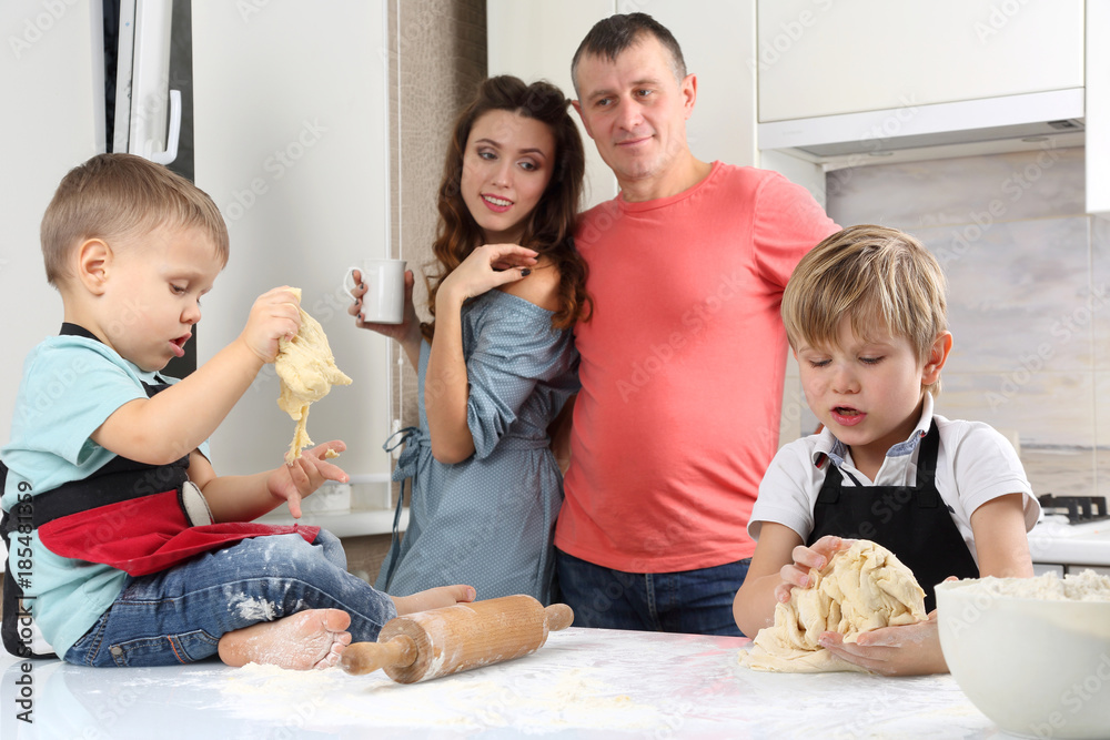 parents look at their young sons, who knead the dough on the kitchen table.