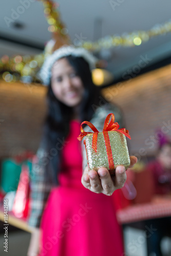 beautiful woman wear red dress and santa claus hat showing golden gift box on hand  in restaurant. concept of Christmas party and New year party.