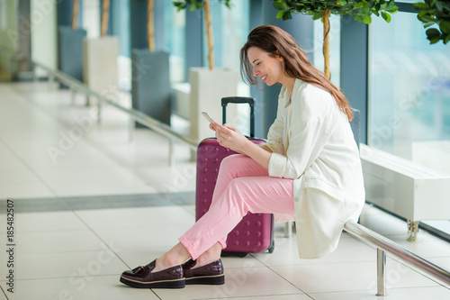 Young woman in international airport with her luggage and smartphone waiting for her flight