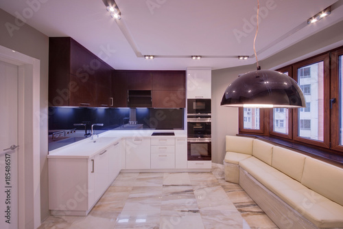 The light big kitchen with light and dark cases  a marble floor and a light sofa  
