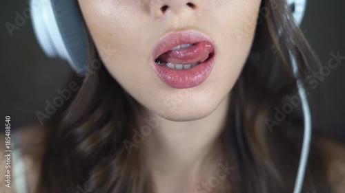 Face of sexy brunette close-up. A young woman in big white headphones is flirting with the camera. eroticly opens his mouth. chubby female lips. 4k