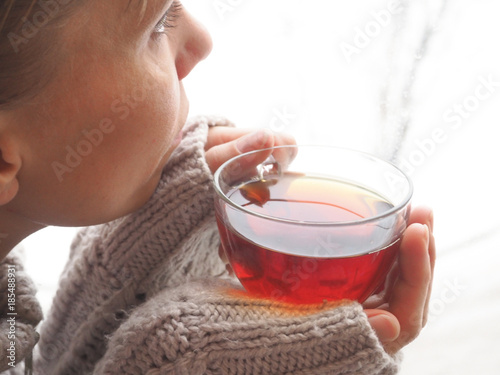 Young girl drinking tea and looking sadly out the window. Winter melancholy. 