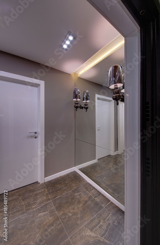 A corridor with a big mirror, lamps and a white door