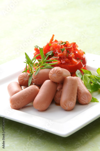 Chicken & Beef cocktail sausage with cherry tomato radish and lemon with green herb with toast bread on green red and bamboo background  with white and green plate