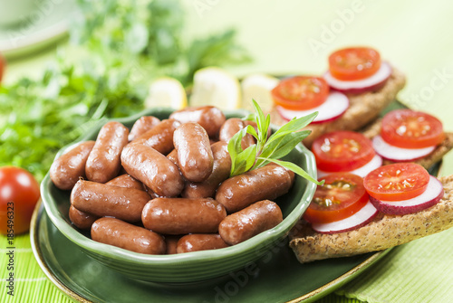 Chicken & Beef cocktail sausage with cherry tomato radish and lemon with green herb with toast bread on green red and bamboo background  with white and green plate