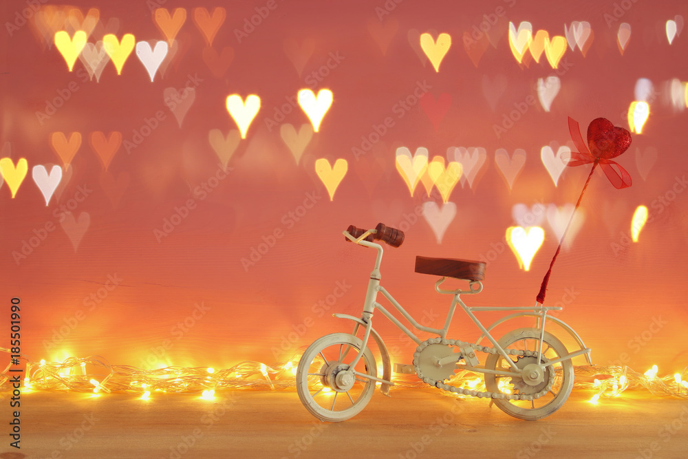 Valentine's day romantic background with white vintage bicycle toy and glitter red heart on it over wooden table.