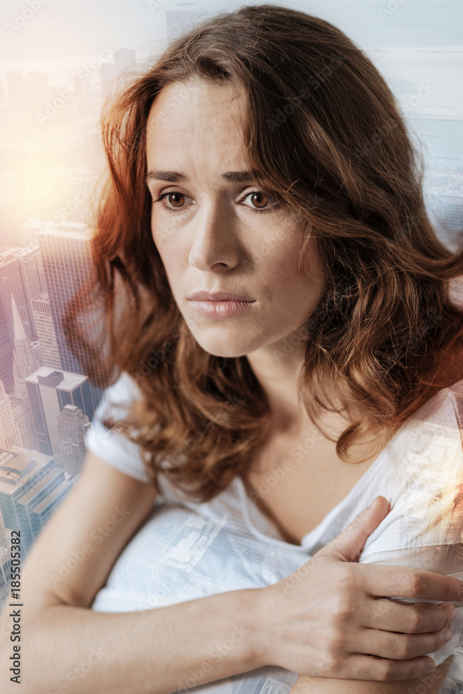 Deep in thoughts. Depressed brunette looking forward, crossing arms while sitting against urban background Deep in thoughts. Depressed brunette looking forward, crossing arms while sitting against urban background