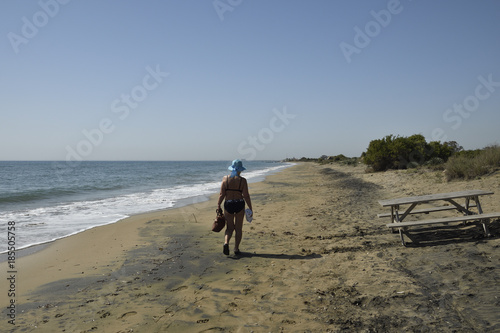 Women in hat and bikini walking at sea shore with blue sky and sea in background