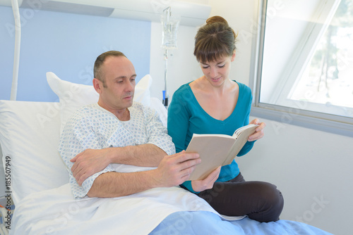 caring wife reading to his husband in hospital