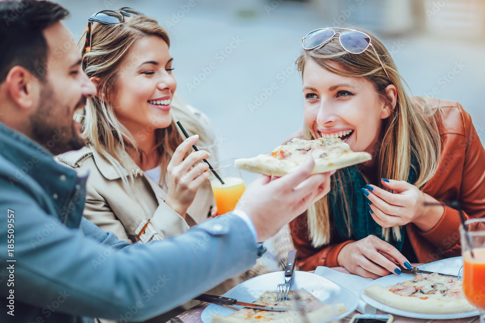 Happy group of friends eating pizza outdoors