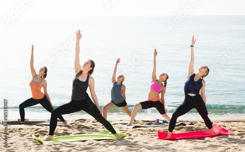 Young concentrated women exercising yoga poses on sunny beach
