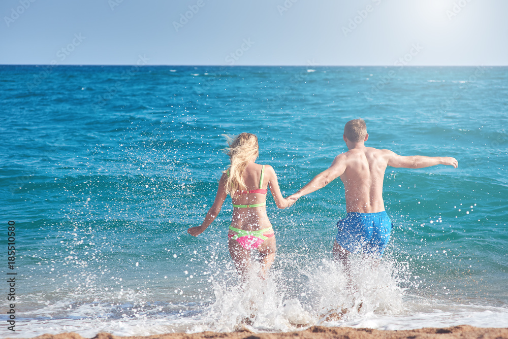 Caucasian couple running into the sea water. Back view. Caucasian couple running into the sea water. Back view.