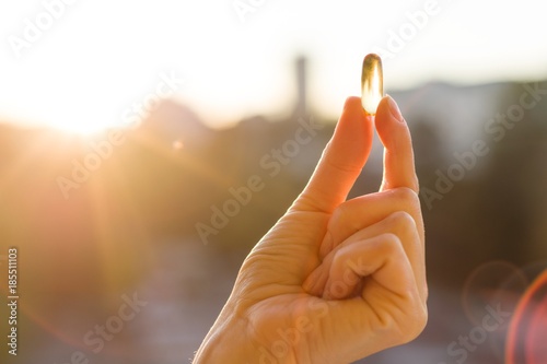 Hand of a woman holding fish oil Omega-3 capsules, urban sunset background. Healthy eating, medicine, health care, food supplements and people concept
