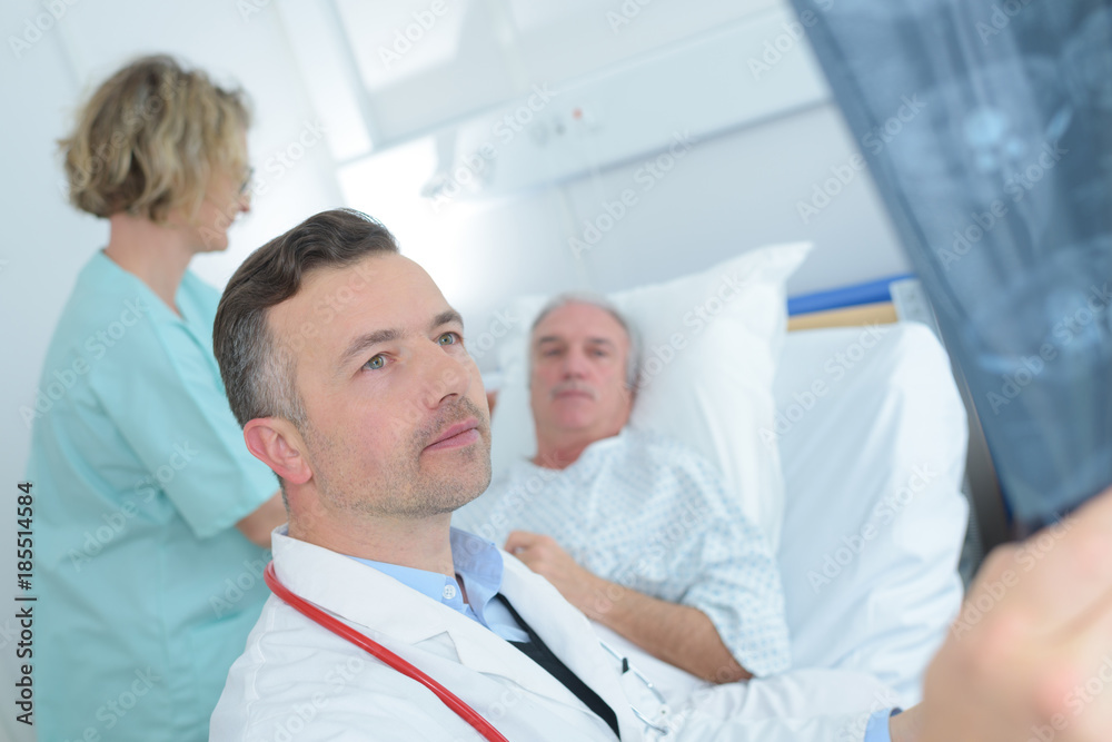 Fototapeta premium male doctor sitting on bed near patient and examining x-ray