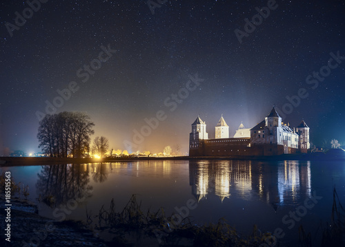 Landscape of Mir Castle in starry night. clear night sky on Mirsky Castle with reflections in lake and city's shining in background, Belarus.