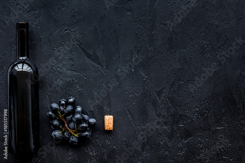 Wine bottle near bunch of black grapes on black background top view copyspace