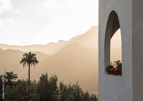 White building with arch window with plants, palm trees and mountains in the background photo